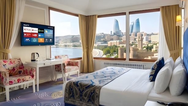 A hotel room with a bed, a desk, a chair, a TV displaying streaming services, and a city view. - Gold Senator Hotel (Baku)