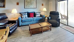 Ein Wohnzimmer mit einer Couch, Sesseln, einem Couchtisch und einem großen Fenster.