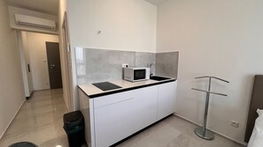 Una kitchenette compacta con microondas, un lavamanos pequeño y un cubo de basura.