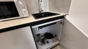 Una cocina con encimera negra, un lavabo blanco, una estufa y un microondas.