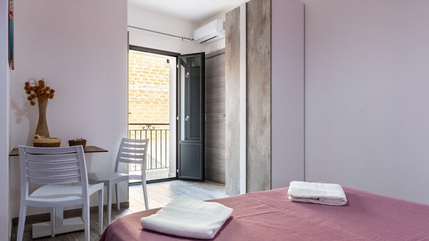 A bedroom with a bed, a small table with chairs, a vase with flowers, and a view of a balcony. - Room 'Perla Marina - Scala Dei Turchi' with Balcony, Wi-Fi, Air Conditioning and Shared Kitchen (Realmonte)