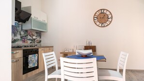 A kitchen with a stove, oven, microwave, and cabinets. There is a dining table with chairs and a wall clock. - Room 'Perla Marina - Scala Dei Turchi' with Balcony, Wi-Fi, Air Conditioning and Shared Kitchen (Realmonte)