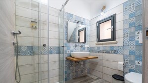 Un bagno con cabina doccia in vetro, lavandino con specchio e WC.