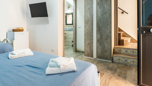 Una camera d'albergo con un letto, una televisione, un bagno visibile attraverso una porta aperta e una scala con gradini decorati.