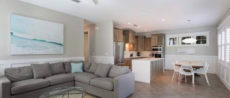 A modern living room with a sectional sofa, a glass coffee table, and a dining area with white chairs.