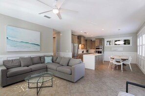 A modern living room with a sectional sofa, a glass coffee table, and a dining area with white chairs. - Villa La Concha~West of Gulf Steps to the Beach! (Anna Maria)