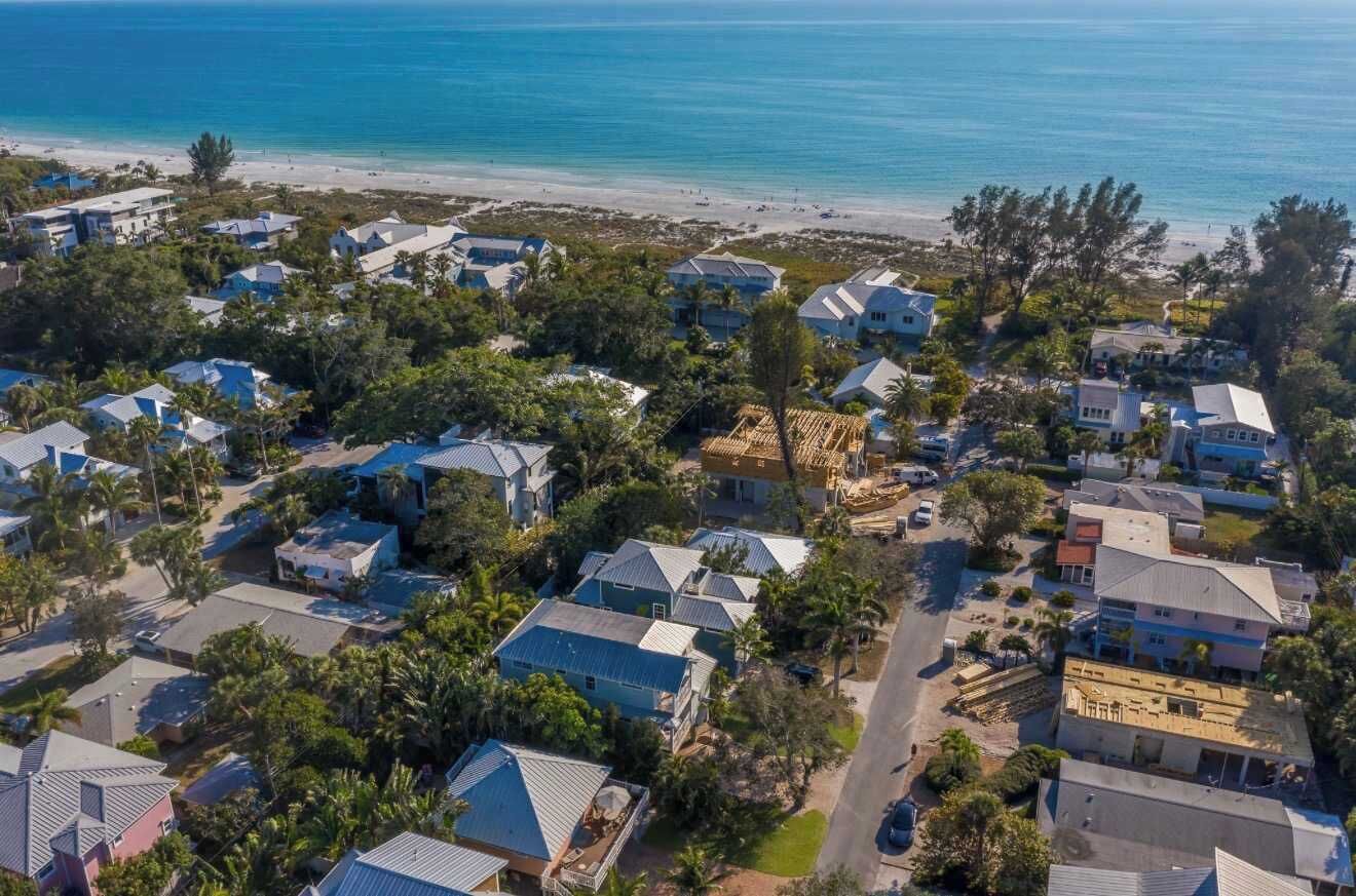 Vue aérienne d’une zone résidentielle côtière, avec des maisons, une plage et un ciel dégagé.