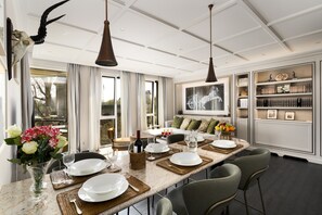 A dining area with a long table set for four, a wine bottle, and a vase of flowers. - Dimora Elvezia Milano (Milan)