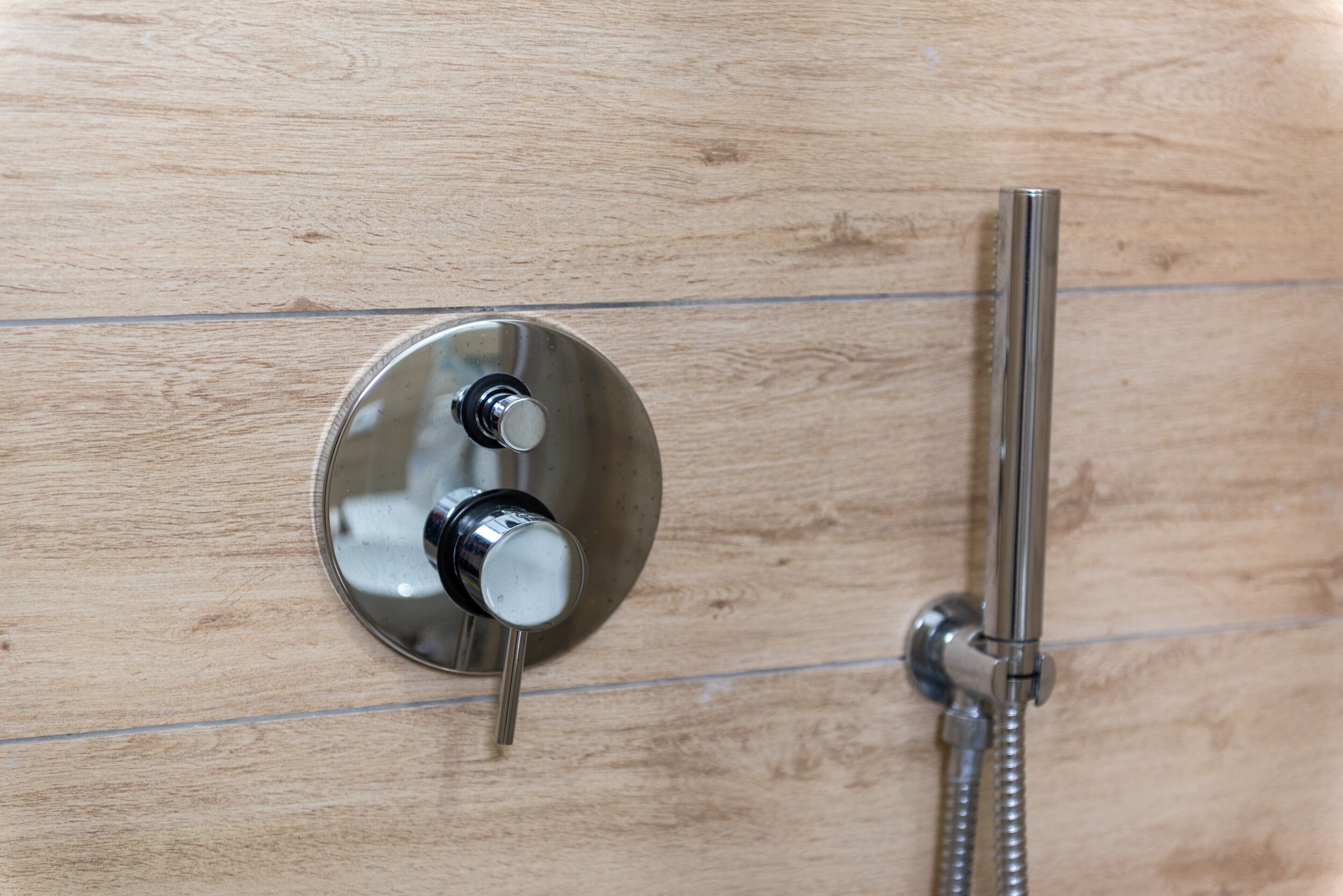 A shower control panel with a handheld showerhead and a wall-mounted faucet.