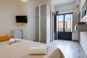 A hotel room with a bed, a flat-screen TV, a wardrobe, a balcony with a view of buildings, and a basket on the wall. - Room 'Perla Marina - U Scogliu' with Balcony, Wi-Fi, Air Conditioning and Shared Kitchen (Realmonte)