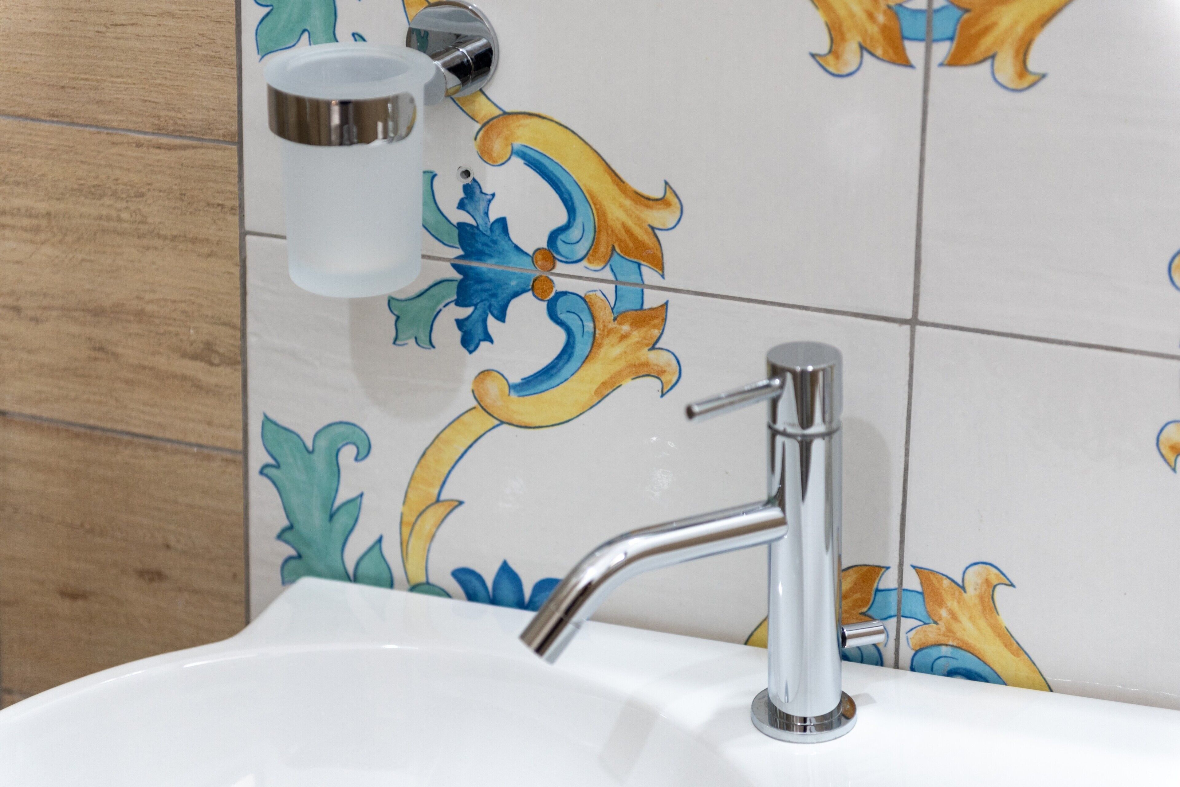 Un lavamanos con grifo cromado, dispensador de jabón y azulejos decorativos con motivos florales.