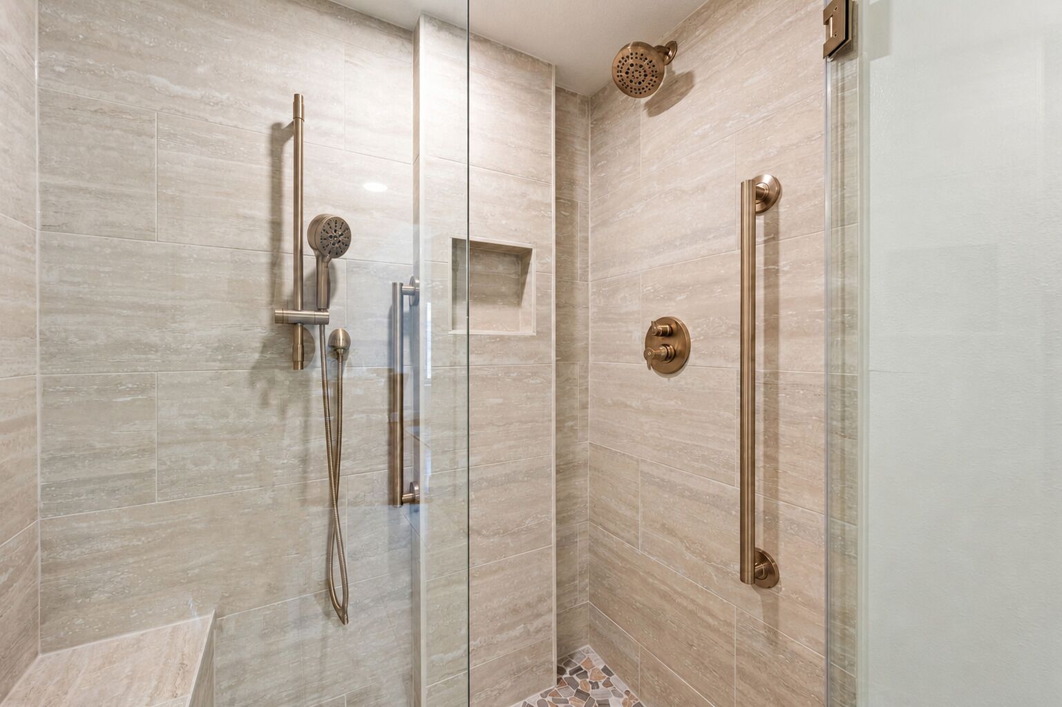 A modern shower with a glass door, a handheld showerhead, and a wall-mounted control panel.