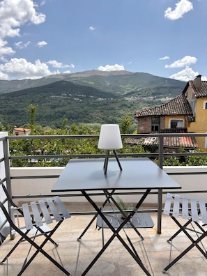 Una terraza con una mesa y sillas, una lámpara y vistas a montañas y un pueblo.