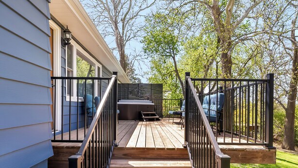 Eine Holzterrasse mit Metallgeländer, die zu einer überdachten Sitzgelegenheit im Freien führt.