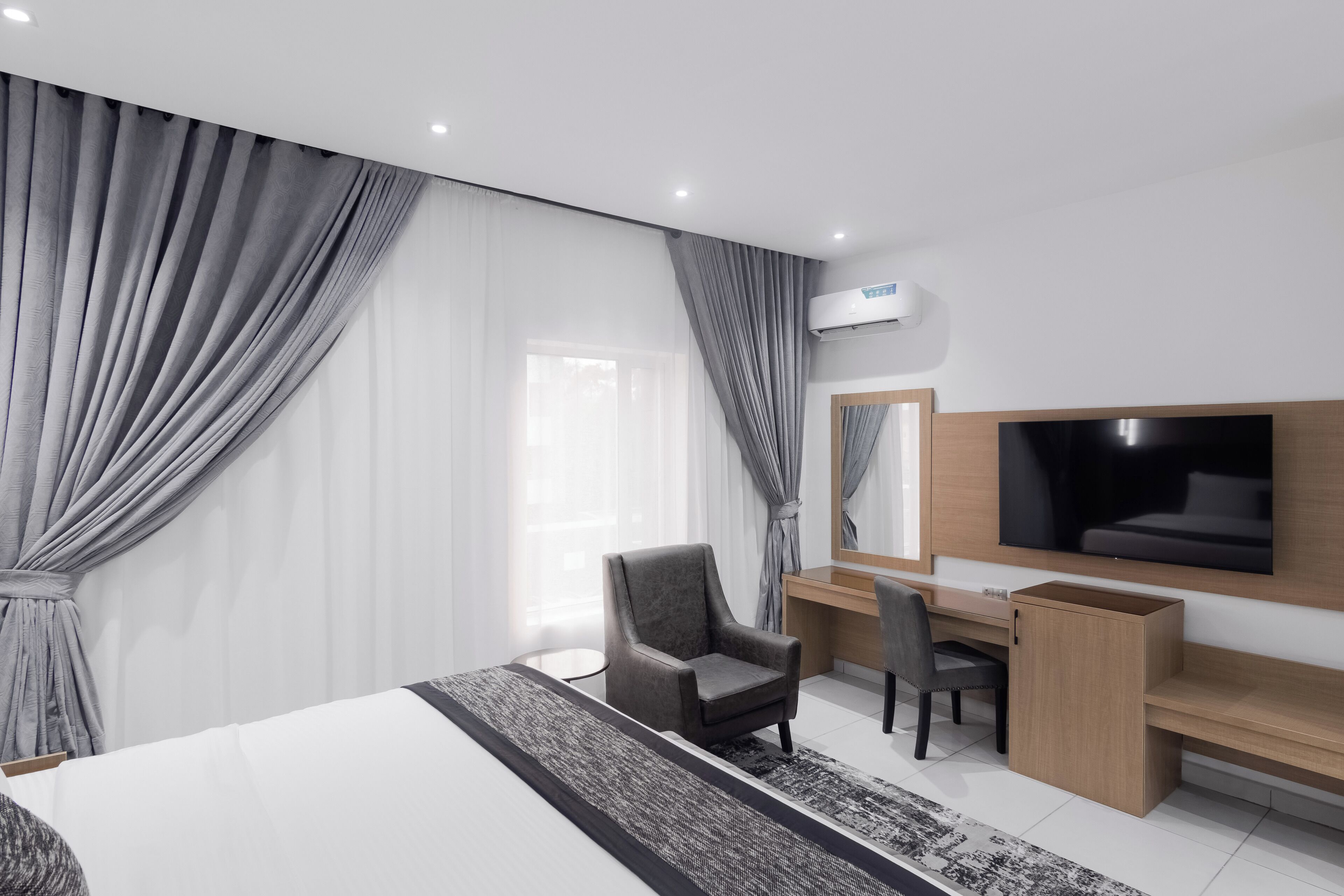 Ein modernes Hotelzimmer mit einem großen Bett, einem Schreibtisch, einem Sessel, einem Fernseher und einer Klimaanlage.
