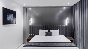 Una habitación de hotel moderna con una cama grande, cabecera con iluminación integrada, mesita de noche y un cuadro enmarcado en la pared.