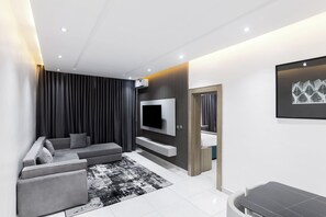 A modern living room with a sectional sofa, flat-screen TV, and a minimalist design. - BON Hotel Conservation Lekki (Lekki)