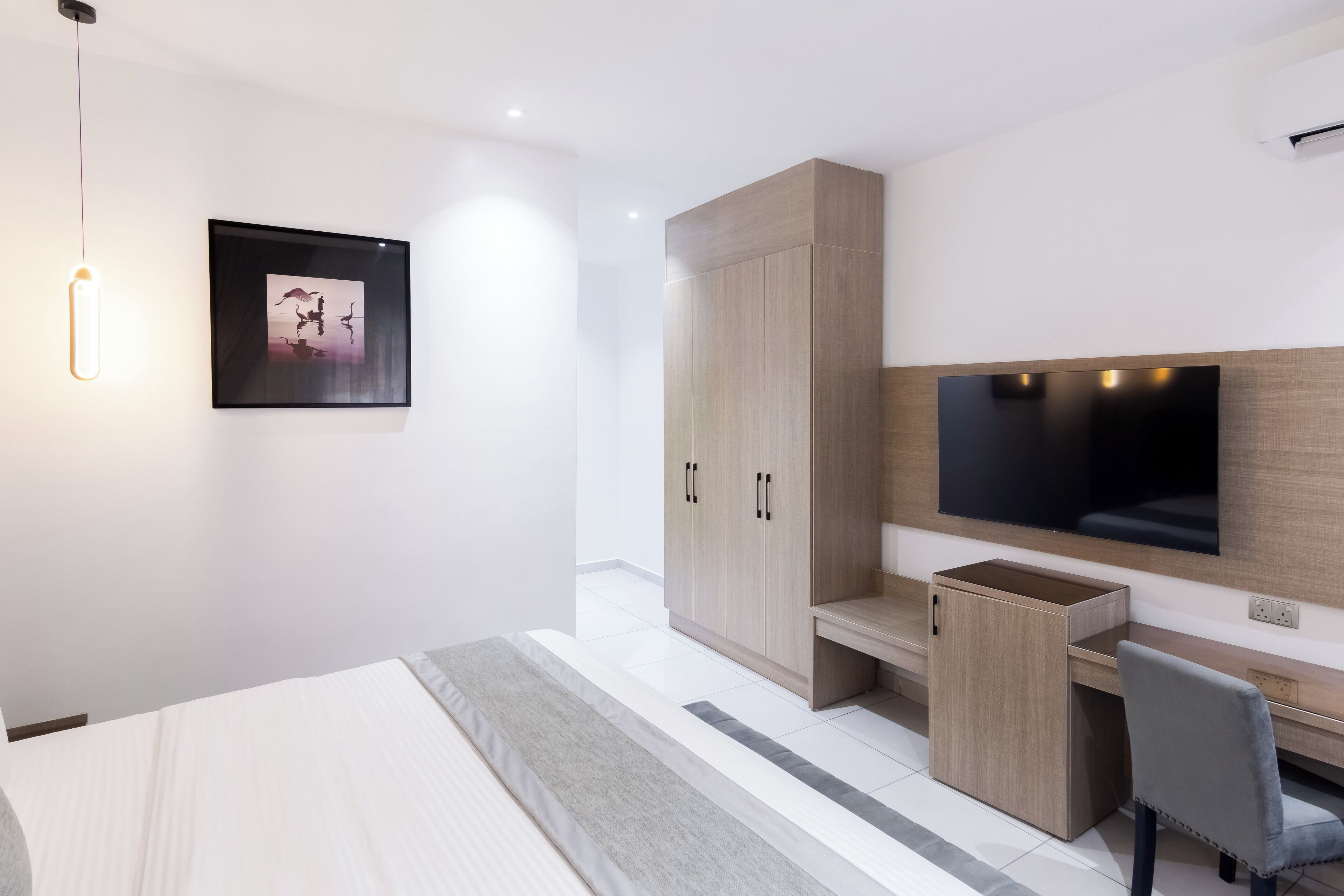 Une chambre d’hôtel moderne équipée d’un lit, d’un bureau, d’une chaise, d’une télévision et d’une armoire.