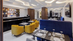 En modern restaurang med en bar, gula och blå sittplatser och ett väl upplyst tak.