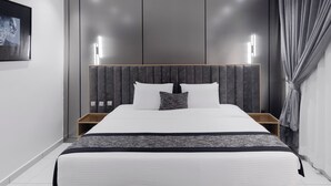 Ett modernt hotellrum med en stor säng, en sänggavel i trä, sängbord och en inramad tavla på väggen.