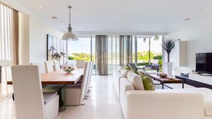 A modern living room with a dining area, a sofa set, a TV, and a large window with a view.