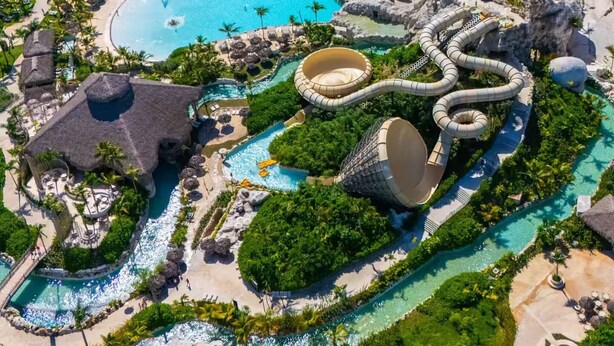 An aerial view of a resort with multiple swimming pools, water slides, and lush greenery.