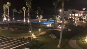 Et resort om natten med swimmingpool, palmer og veloplyste stier.