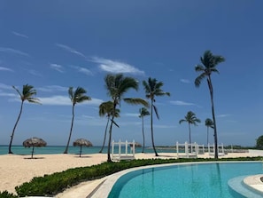 Ein Pool, umgeben von Palmen, und ein Strand mit einer Umzäunung.