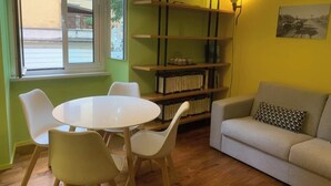 Ein Zimmer mit einem runden Tisch, vier Stühlen, einem Sofa, einem Bücherregal und einem Fenster.