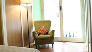 Ein Zimmer mit einem grünen Sessel, einer Stehlampe und einer Schiebeglastür, die zu einem Außenbereich führt.