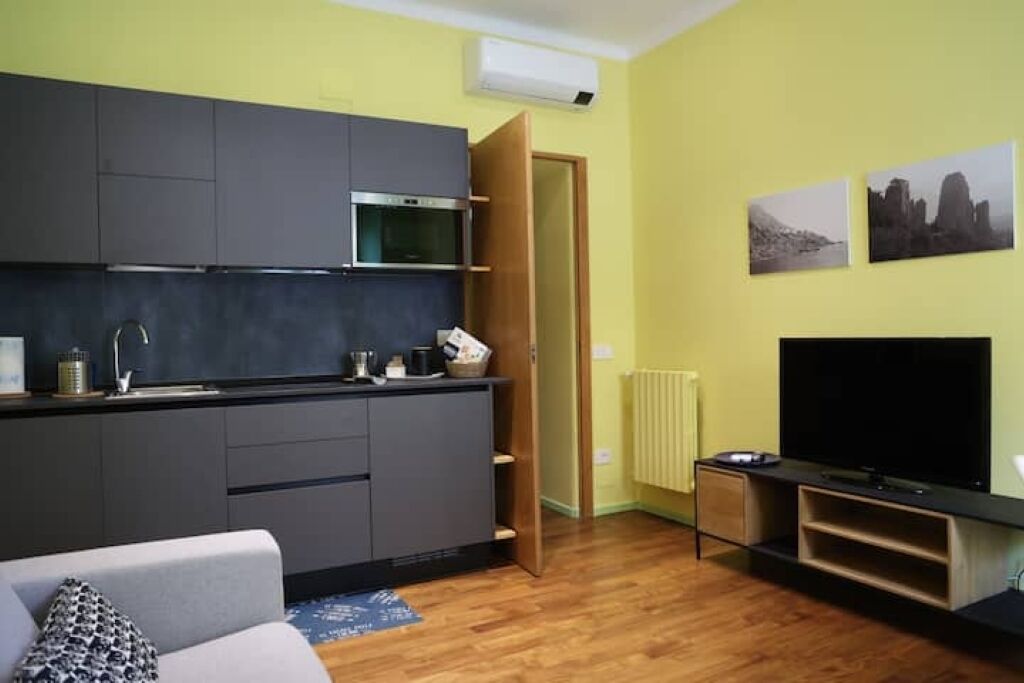Un espacio habitable compacto con kitchenette, un sofá, televisión de pantalla plana y obras de arte en las paredes.
