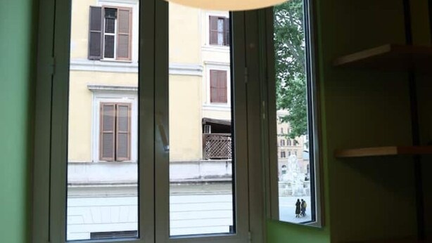 Ein Zimmer mit Fensterblick auf eine Straße, einer grünen Wand und einem hölzernen Regal.