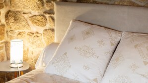 A bed with patterned pillows, a bedside lamp, and a stone wall. - Breton Character House with Shared Pool (Ergué-Gabéric)
