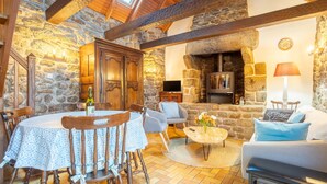 A stone-walled room with a wooden table and chairs, a sofa, a fireplace, and a television. - Breton Character House with Shared Pool (Ergué-Gabéric)