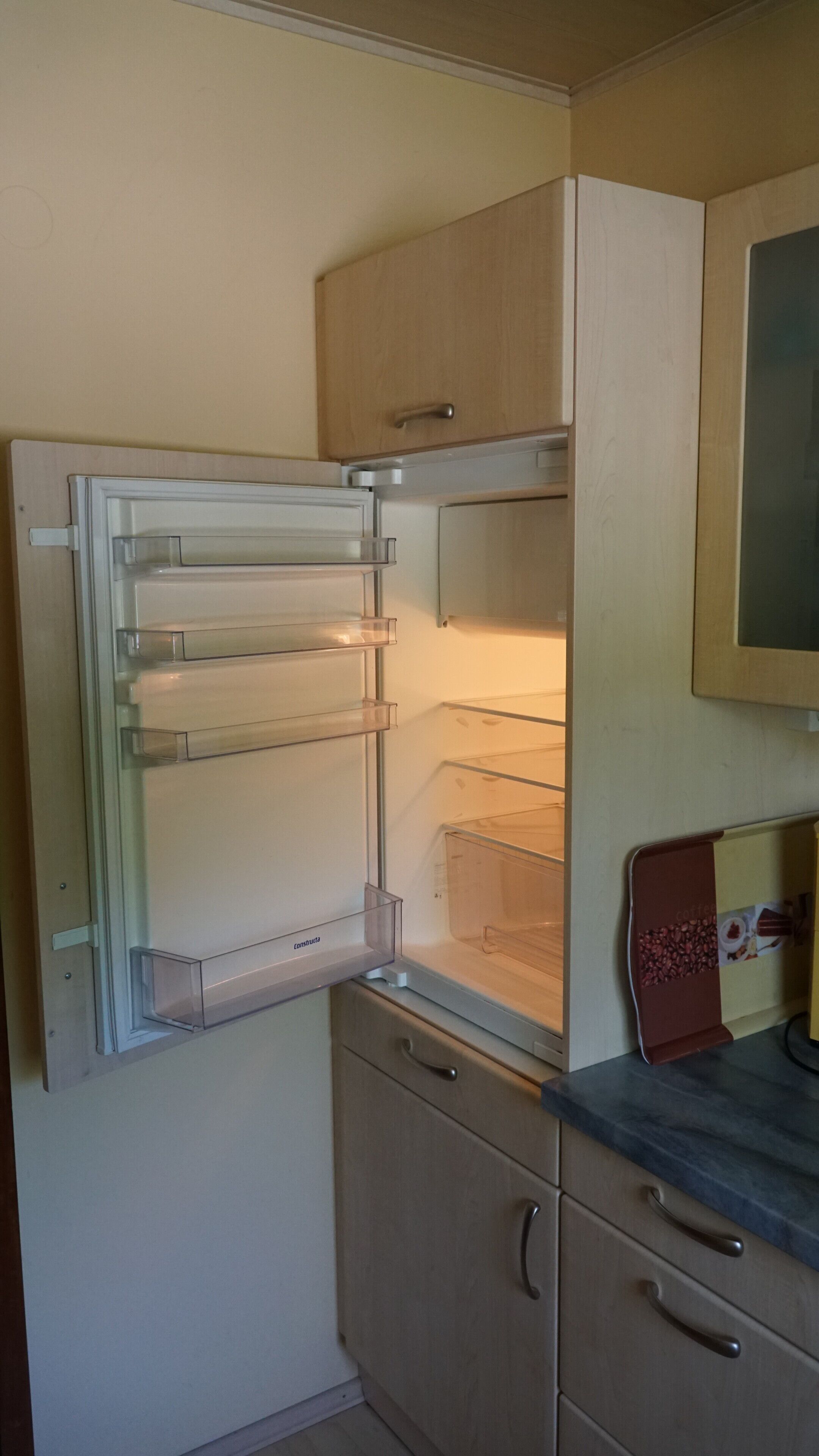 Una cocina con refrigerador empotrado, un mueble de madera y una encimera con cafetera.