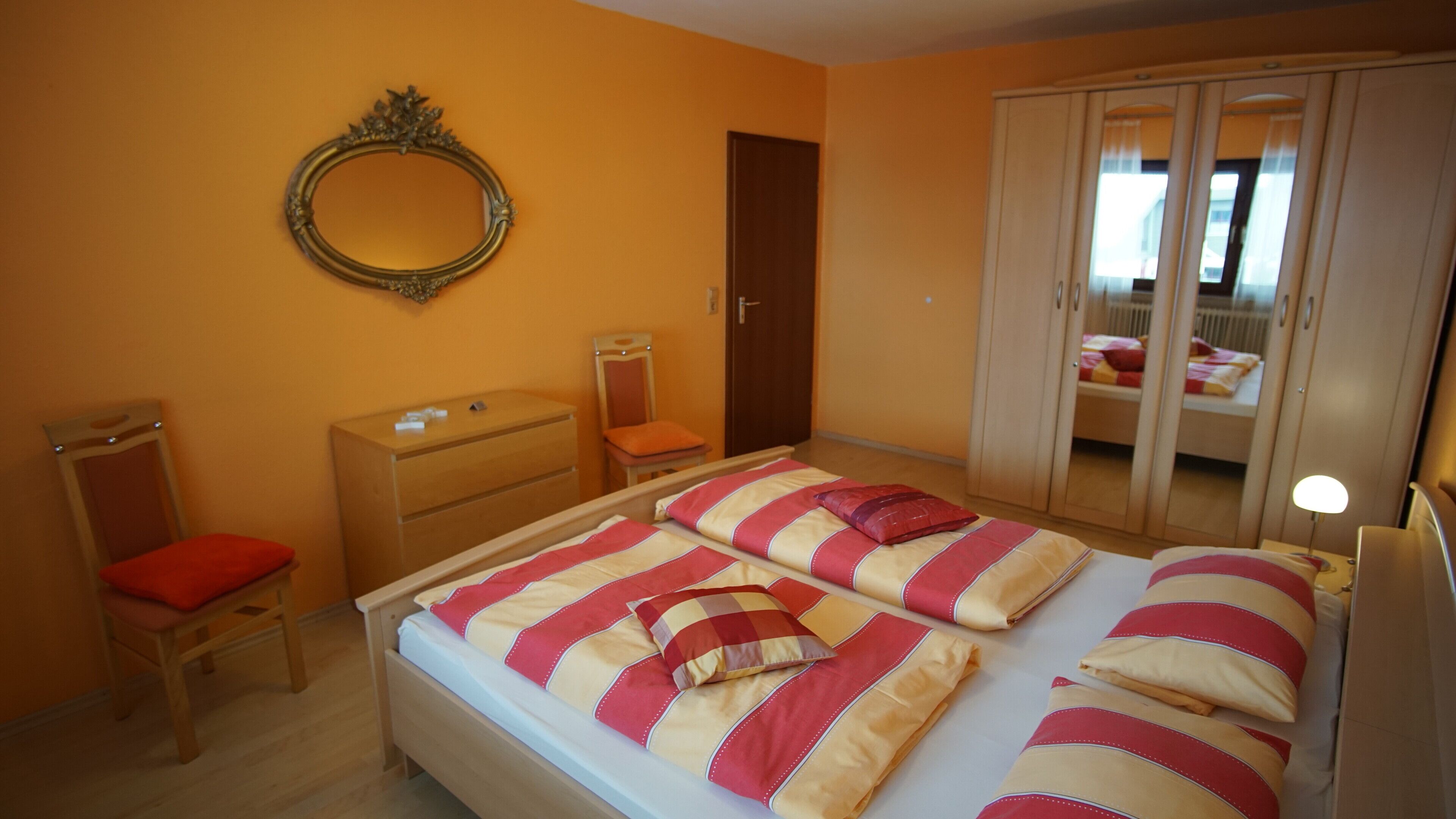 Un dormitorio con cama, cómoda, silla, armario y espejo.