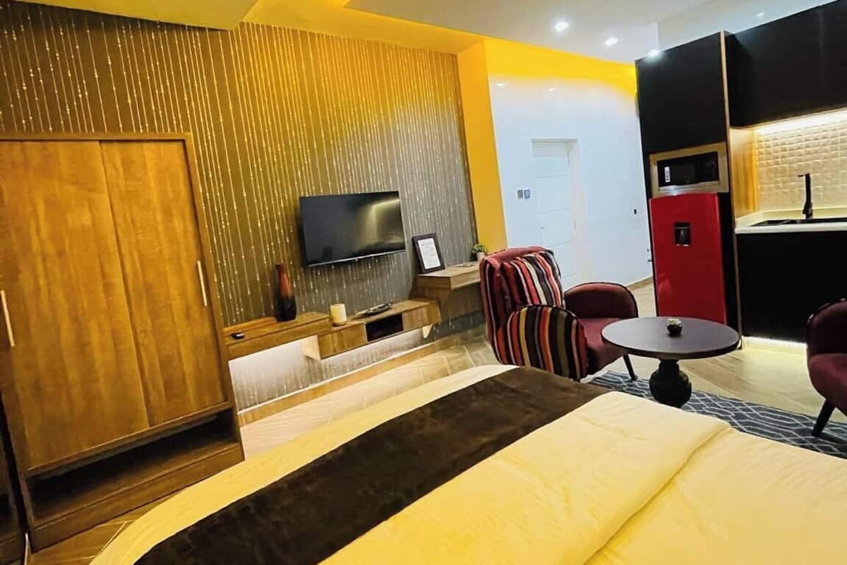 A hotel room with a bed, a TV, a minibar, a desk, and a seating area.
