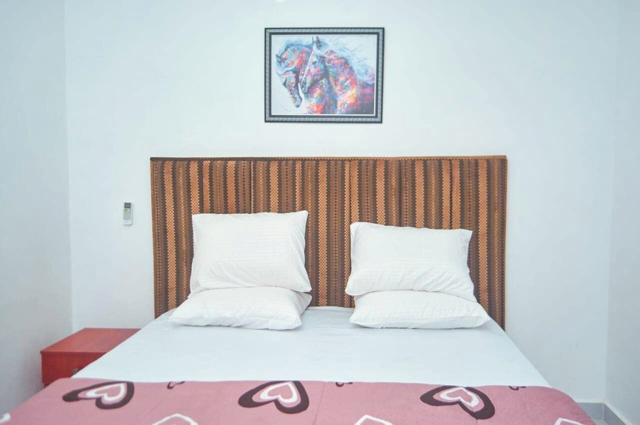Una cama con cabecera a rayas, dos almohadas, una mesita de noche roja y un cuadro enmarcado sobre la cama.