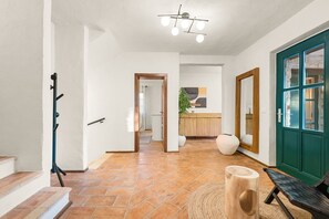 Ein Flur mit Kleiderhaken, einer Holzbank, einer großen Vase und einer grünen Tür.