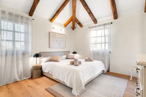 Ein Schlafzimmer mit Holzboden, einem Bett mit weißer Bettwäsche, zwei Nachttischlampen und einem Teppich mit Fischgrätenmuster.