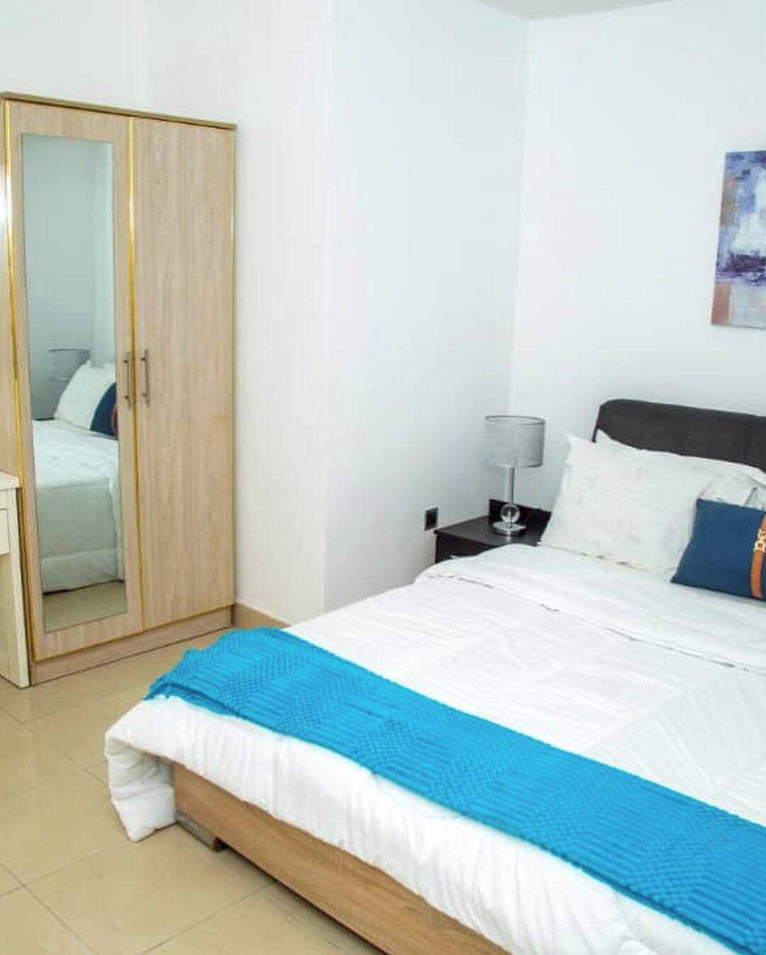 A bedroom with a bed, a wardrobe, a nightstand, and a lamp.