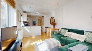 Ein modernes Wohnzimmer mit einem grünen Sofa, einem Esstisch und einer Küche im Hintergrund.