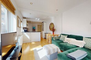Ein modernes Wohnzimmer mit einem grünen Sofa, einem Esstisch und einer Küche im Hintergrund.