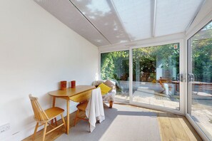 Ein modernes Zimmer mit einem Holztisch und -stühlen, einer Glastür zu einem Außenbereich und einer weißen Decke.