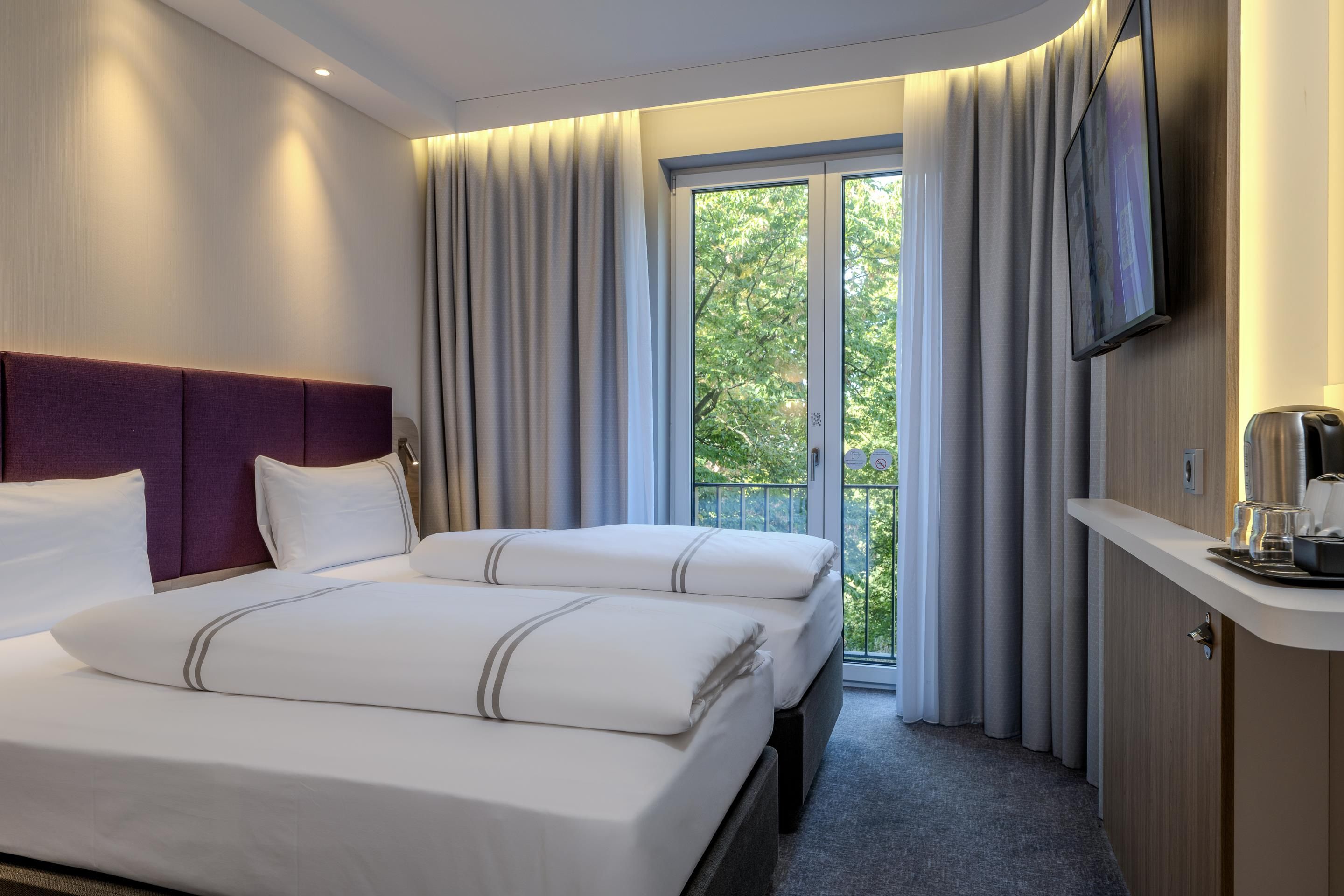 Quarto de hotel com cama, televisão e varanda com cortinas.