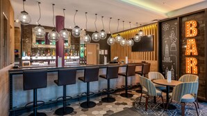 A bar area with multiple stools and a round table, a bar counter with bottles, and a wall with illuminated letters.
