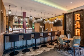 A bar area with multiple stools and a round table, a bar counter with bottles, and a wall with illuminated letters.