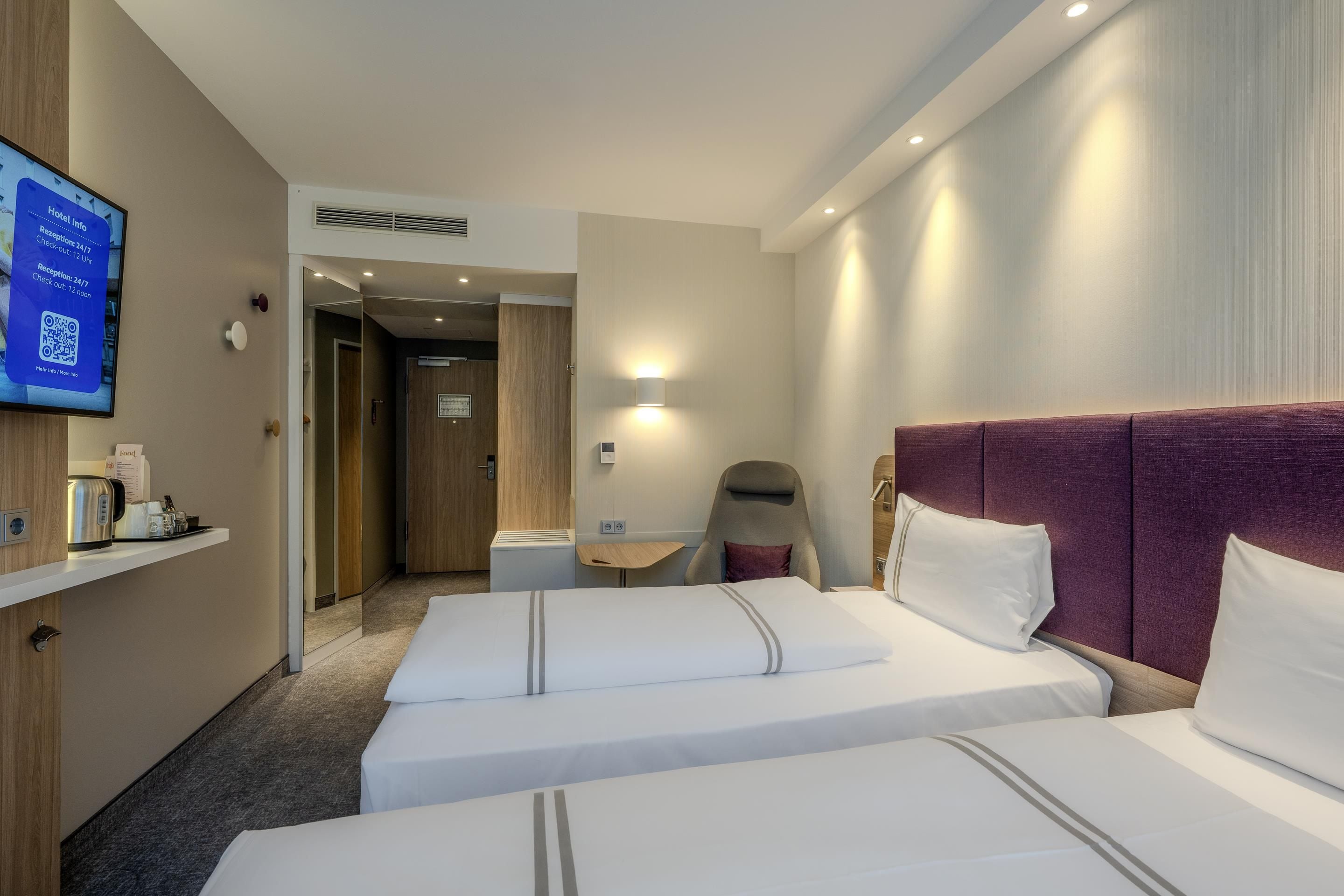 Quarto de hotel com duas camas, uma mesa de trabalho, uma cadeira e uma televisão exibindo informações do hotel.