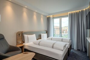 A hotel room with a bed, a chair, a desk, and a window with curtains.