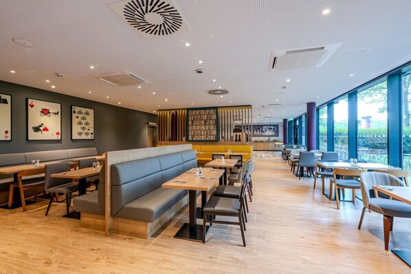 A restaurant with wooden tables, grey and yellow booths, and large windows offering a view.
